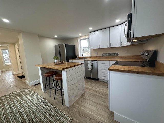 kitchen with appliances with stainless steel finishes, butcher block counters, light hardwood / wood-style flooring, and white cabinetry