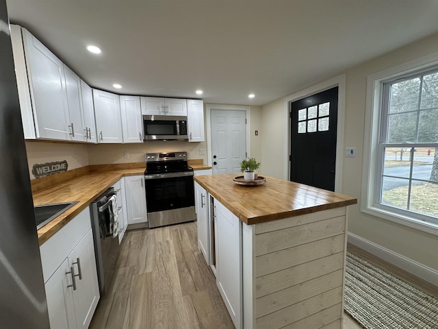 kitchen with wooden counters, light hardwood / wood-style floors, a center island, white cabinetry, and appliances with stainless steel finishes