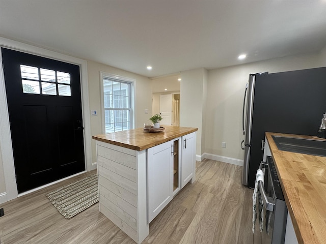 kitchen with light hardwood / wood-style floors, wooden counters, a kitchen island, white cabinets, and dishwashing machine