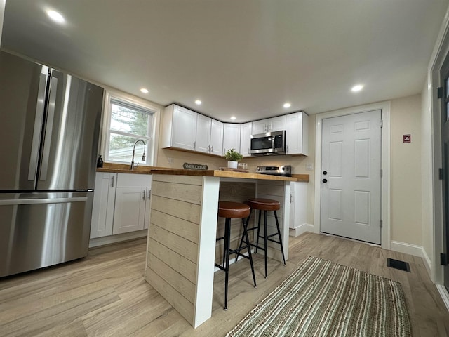 kitchen with white cabinets, appliances with stainless steel finishes, light hardwood / wood-style floors, a kitchen breakfast bar, and butcher block countertops