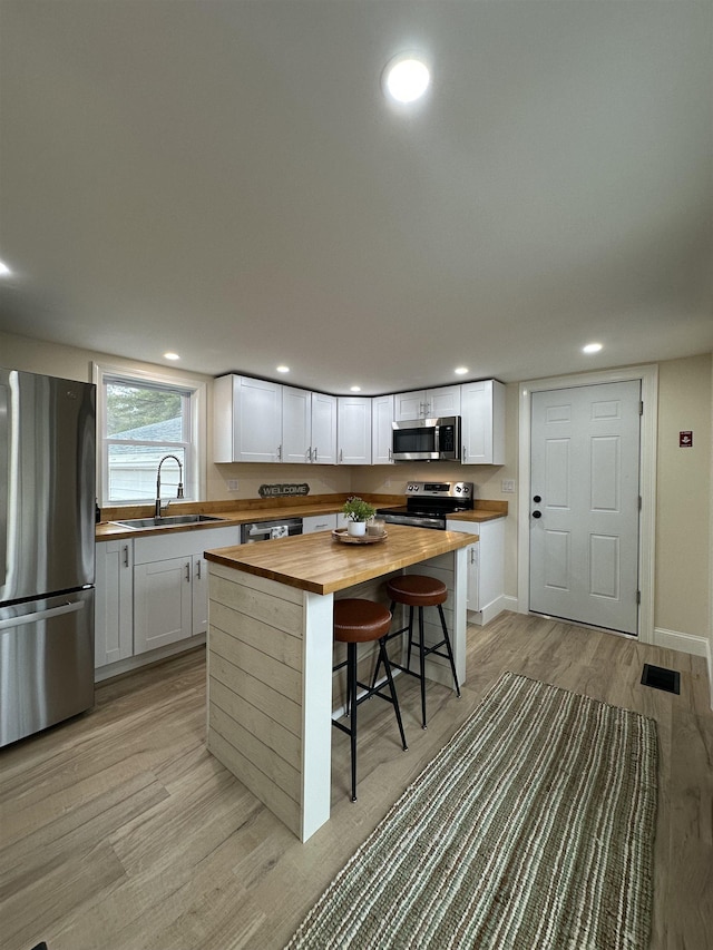 kitchen with butcher block countertops, a kitchen bar, sink, white cabinetry, and appliances with stainless steel finishes