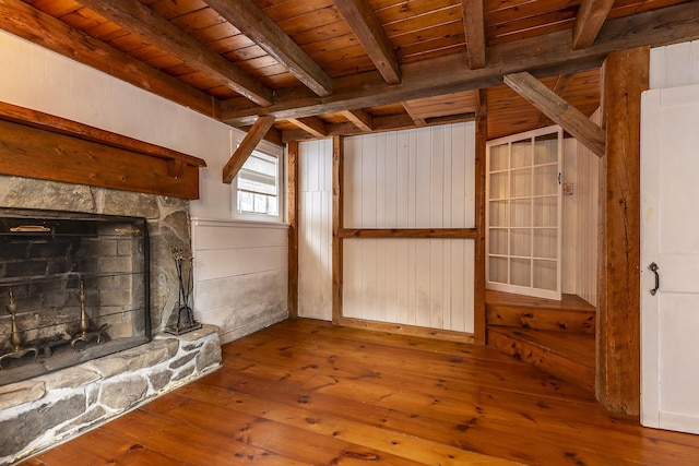 unfurnished living room with wood walls, beam ceiling, wood-type flooring, a stone fireplace, and wooden ceiling