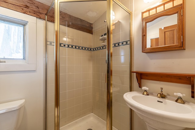 bathroom featuring toilet, a shower with shower door, and sink