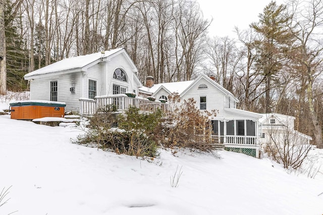 view of snow covered exterior featuring a deck, a sunroom, and a hot tub