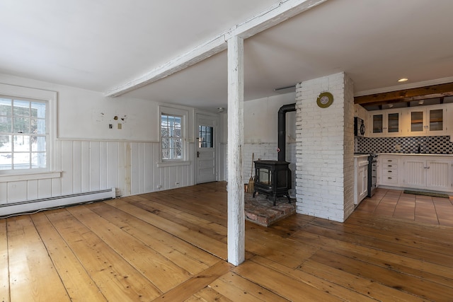 unfurnished living room featuring light wood-type flooring, baseboard heating, and a wood stove