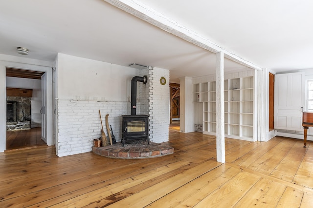 unfurnished living room featuring light hardwood / wood-style floors, a wood stove, and a baseboard heating unit