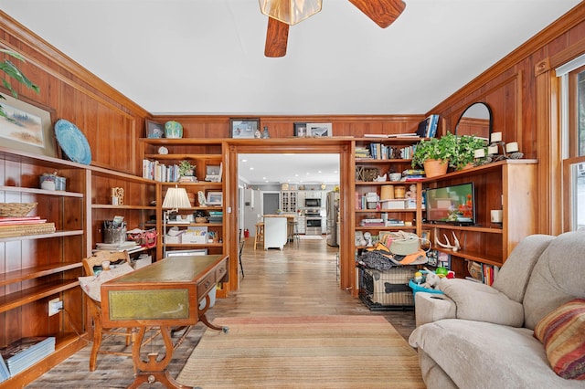 office space featuring ceiling fan, wood walls, crown molding, light hardwood / wood-style flooring, and built in shelves