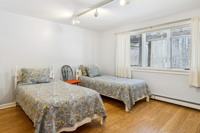 bedroom with wood-type flooring, track lighting, and a baseboard heating unit