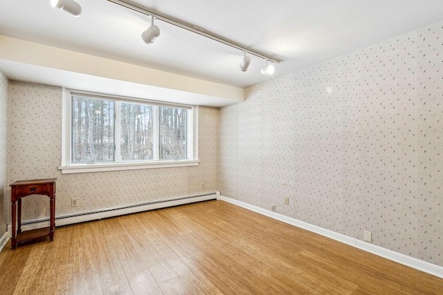 empty room featuring rail lighting, a baseboard heating unit, and hardwood / wood-style floors