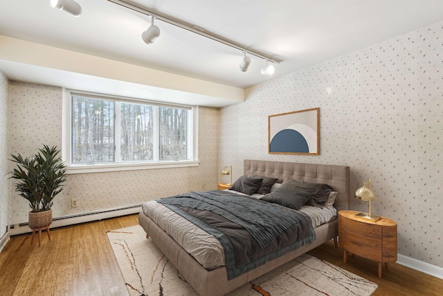 bedroom featuring hardwood / wood-style flooring, baseboard heating, and rail lighting