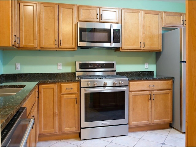 kitchen featuring light tile patterned floors, appliances with stainless steel finishes, and dark stone counters