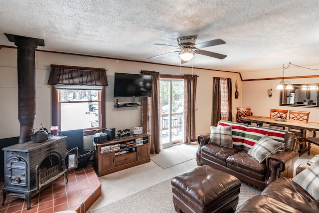 living room with ceiling fan, carpet floors, a textured ceiling, a wood stove, and ornamental molding