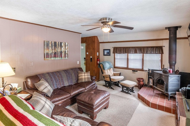 carpeted living room with wooden walls, ceiling fan, a wood stove, a textured ceiling, and ornamental molding