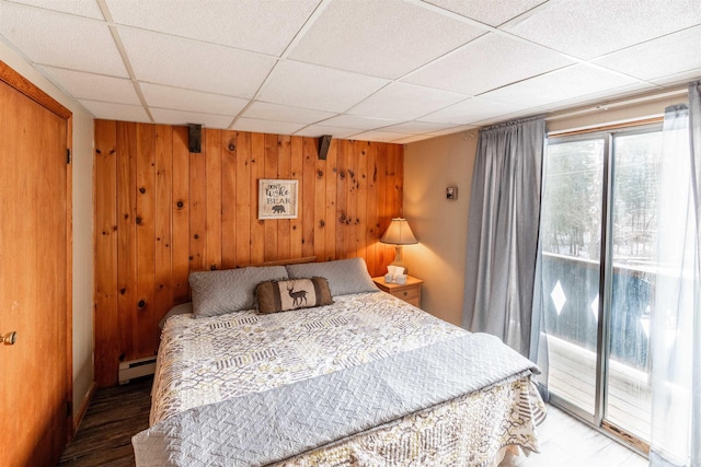 bedroom featuring baseboard heating, a closet, wood walls, and a paneled ceiling