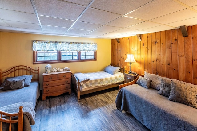 bedroom with a drop ceiling, dark hardwood / wood-style flooring, and wooden walls