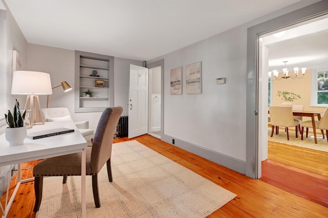 office area with a notable chandelier, radiator heating unit, built in features, and light wood-type flooring