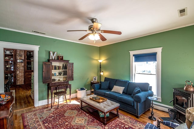 living room with ceiling fan, crown molding, hardwood / wood-style flooring, a wood stove, and baseboard heating