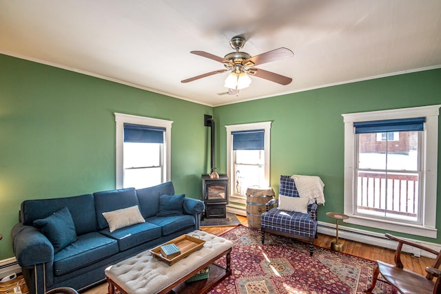 living room with hardwood / wood-style floors, ceiling fan, a wood stove, a baseboard radiator, and ornamental molding