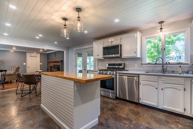 kitchen with appliances with stainless steel finishes, white cabinetry, sink, backsplash, and hanging light fixtures