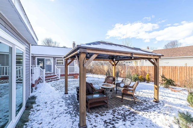 snow covered patio featuring a wooden deck, a gazebo, and an outdoor fire pit