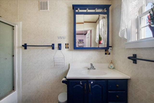 bathroom featuring bath / shower combo with glass door, tile walls, and vanity