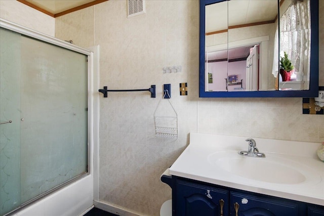 bathroom featuring enclosed tub / shower combo, tile walls, and vanity