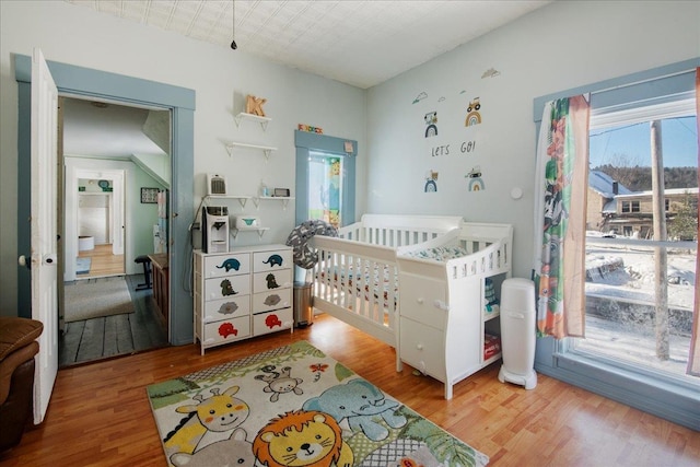 bedroom with multiple windows, light hardwood / wood-style flooring, and a crib