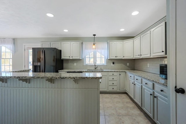 kitchen with tasteful backsplash, black fridge, sink, hanging light fixtures, and white cabinets