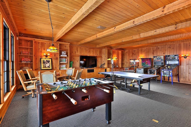 game room featuring wooden walls, wooden ceiling, dark colored carpet, beamed ceiling, and built in shelves