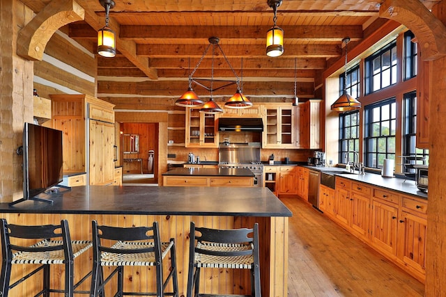 kitchen featuring a breakfast bar area, appliances with stainless steel finishes, beam ceiling, and decorative light fixtures