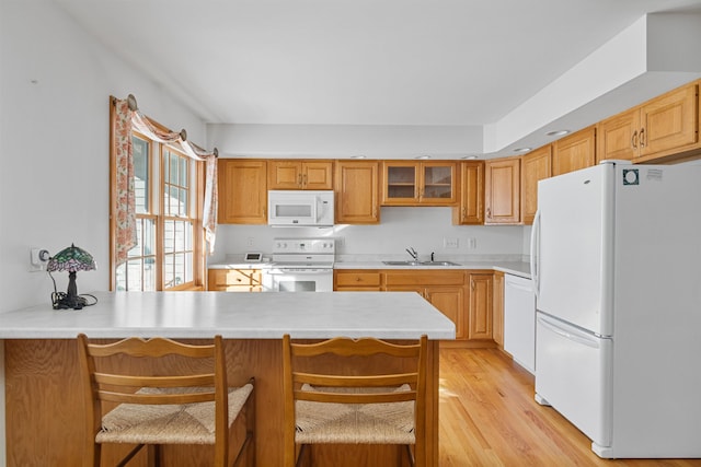 kitchen with sink, a breakfast bar area, kitchen peninsula, white appliances, and light hardwood / wood-style flooring