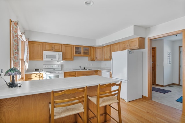 kitchen with sink, white appliances, a kitchen breakfast bar, kitchen peninsula, and light wood-type flooring