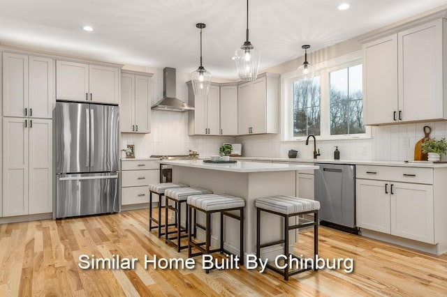 kitchen with light hardwood / wood-style floors, hanging light fixtures, a kitchen breakfast bar, wall chimney range hood, and stainless steel appliances