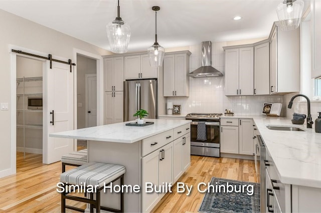 kitchen featuring appliances with stainless steel finishes, a barn door, a center island, wall chimney range hood, and light hardwood / wood-style floors