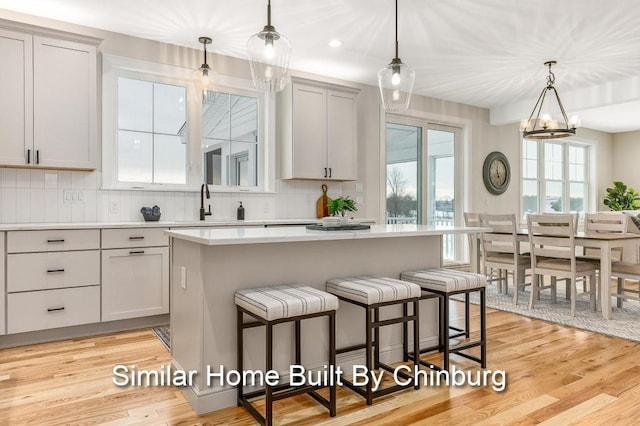 kitchen with decorative light fixtures, light hardwood / wood-style flooring, a center island, and tasteful backsplash