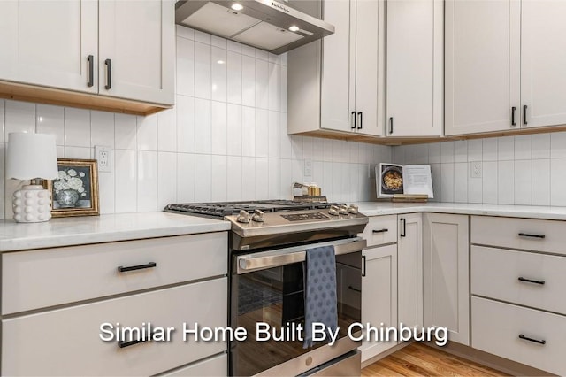 kitchen with stainless steel gas stove, white cabinetry, tasteful backsplash, and wall chimney exhaust hood