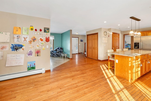 kitchen with baseboard heating, a kitchen island, decorative light fixtures, light wood-type flooring, and light stone counters