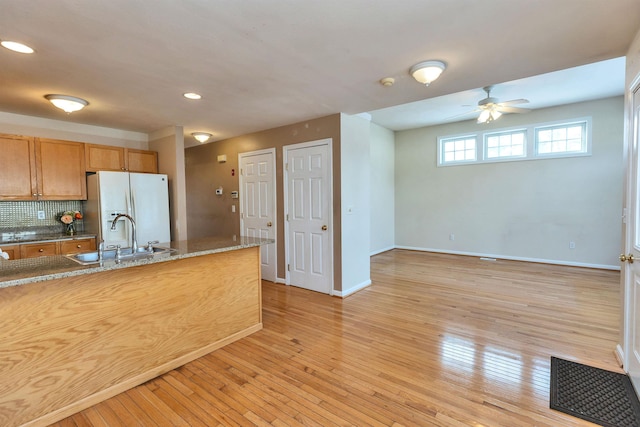 kitchen with white fridge with ice dispenser, light hardwood / wood-style floors, sink, decorative backsplash, and stone counters