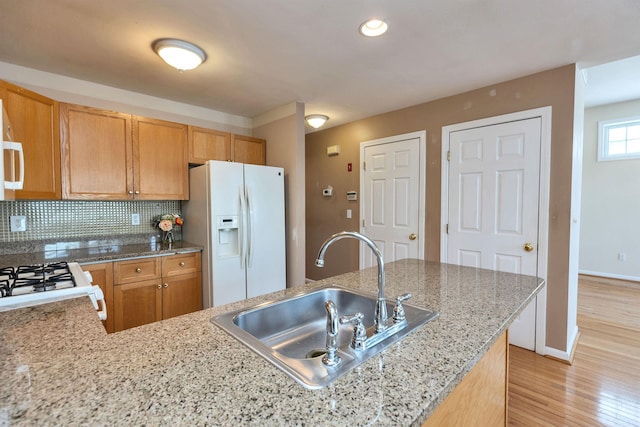 kitchen with white fridge with ice dispenser, tasteful backsplash, light hardwood / wood-style floors, sink, and light stone counters