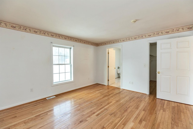 unfurnished bedroom with connected bathroom and light wood-type flooring