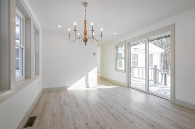 unfurnished dining area with light wood-type flooring, a wealth of natural light, and a notable chandelier