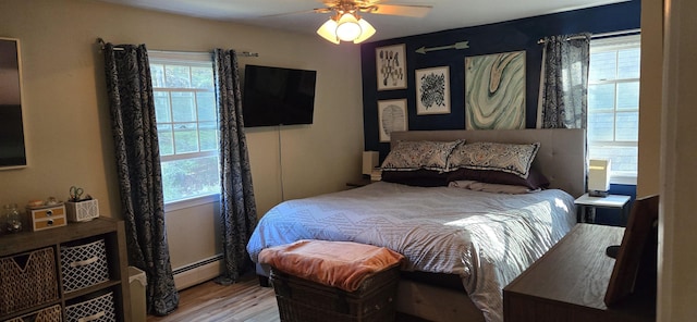 bedroom with wood-type flooring, baseboard heating, multiple windows, and ceiling fan