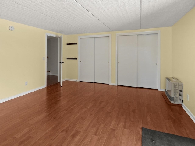 unfurnished bedroom with heating unit, hardwood / wood-style floors, a textured ceiling, and two closets