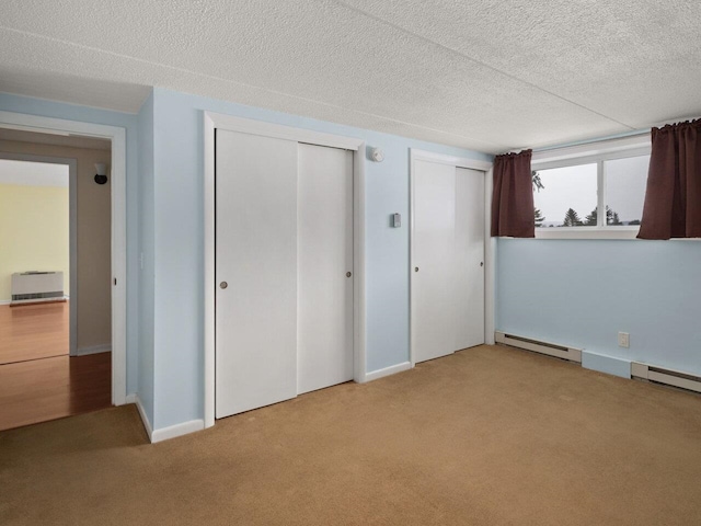 unfurnished bedroom featuring multiple closets, light colored carpet, baseboard heating, and a textured ceiling