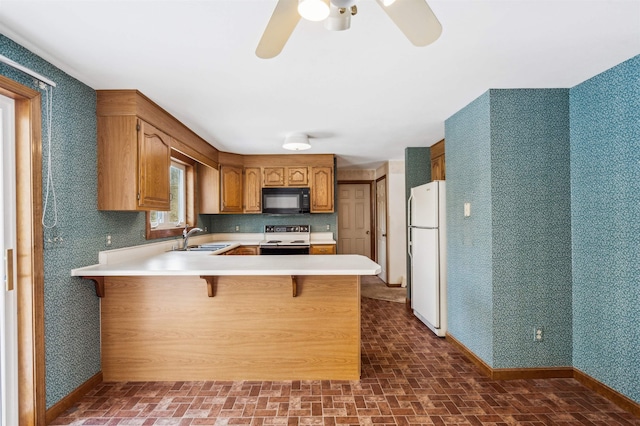 kitchen featuring kitchen peninsula, sink, white refrigerator, range with electric cooktop, and a breakfast bar area