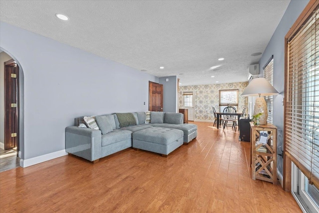 living room with wood-type flooring, a wall mounted AC, and a textured ceiling