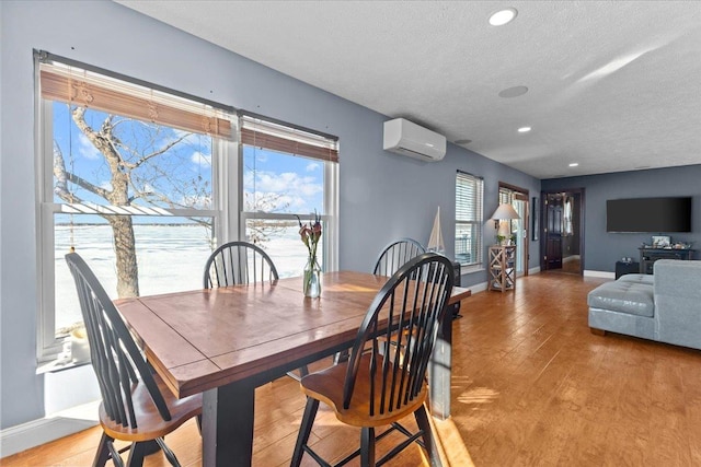 dining room with a water view, a wall mounted AC, light hardwood / wood-style flooring, and a textured ceiling