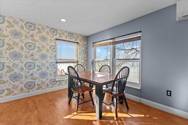 dining space featuring a wealth of natural light, an AC wall unit, light hardwood / wood-style flooring, and a textured ceiling