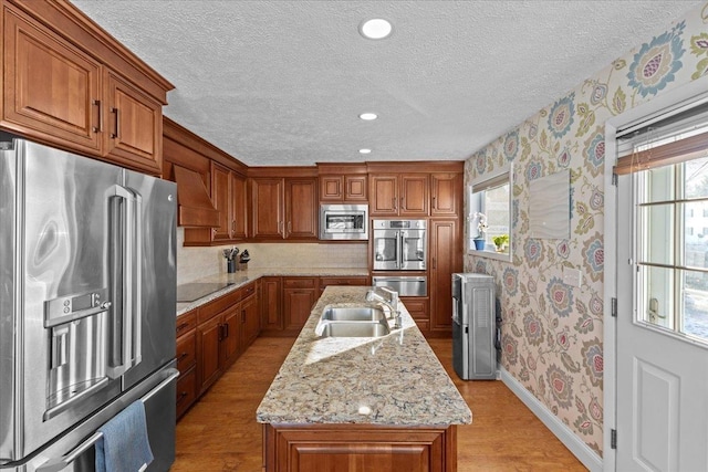 kitchen featuring a wealth of natural light, light stone countertops, appliances with stainless steel finishes, sink, and an island with sink