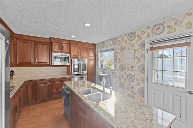 kitchen featuring light stone countertops, sink, appliances with stainless steel finishes, and light hardwood / wood-style floors